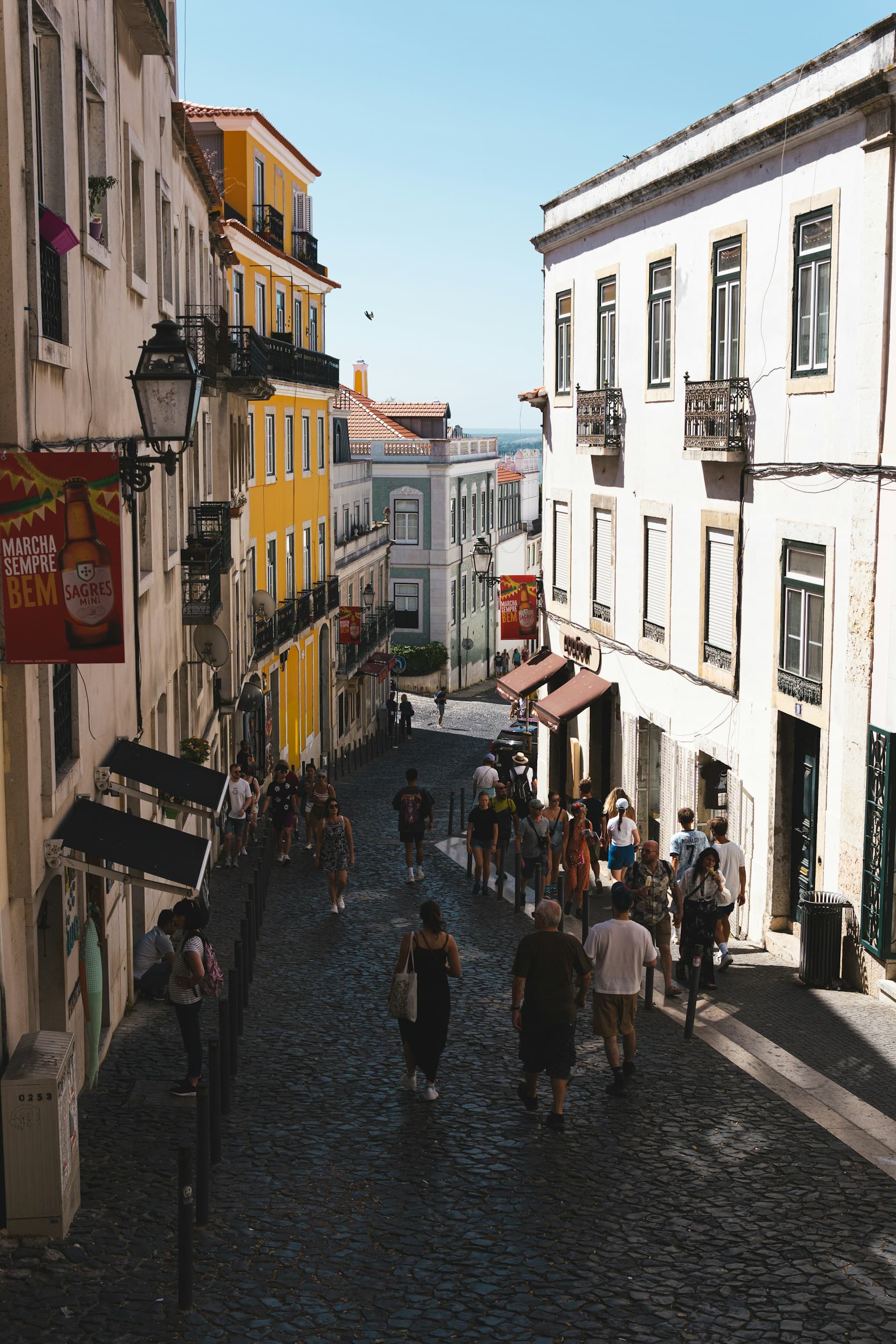 People strolling down a sunlit cobbled street in Alfama, Lisbon